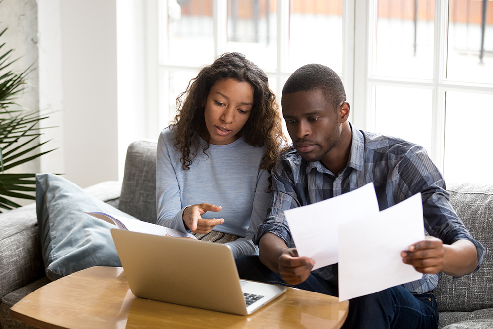 Serious couple discussing paper documents, sitting together on couch at home.